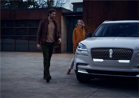 A man and a woman approaching a 2023 Lincoln Aviator® SUV, which illuminates certain lights when they are close | Brinson Lincoln of Corsicana in Corsicana TX