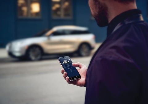 A person is shown interacting with a smartphone to connect to a Lincoln vehicle across the street. | Brinson Lincoln of Corsicana in Corsicana TX